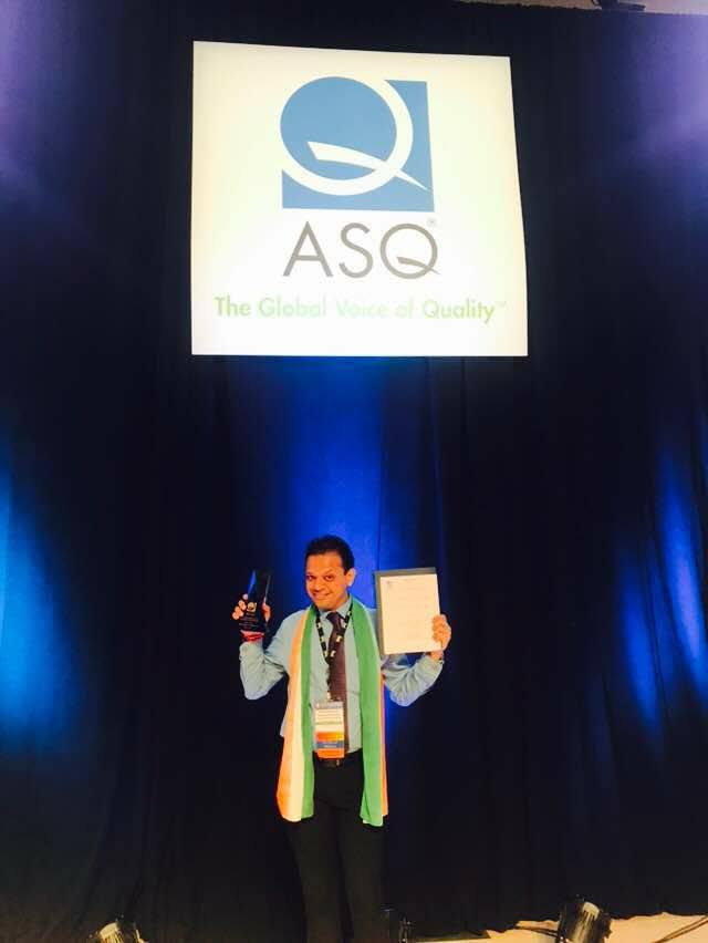 An award winner holding a trophy and certificate on stage beneath the ASQ logo