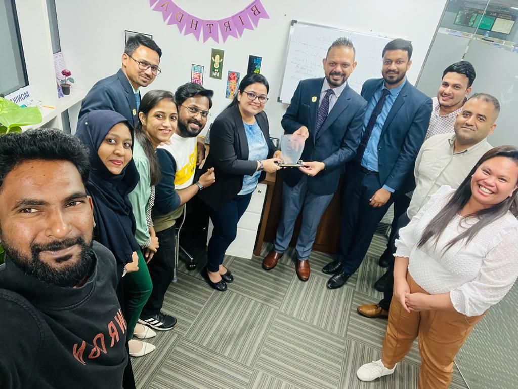 An office team gathered around a glass trophy for a group photo