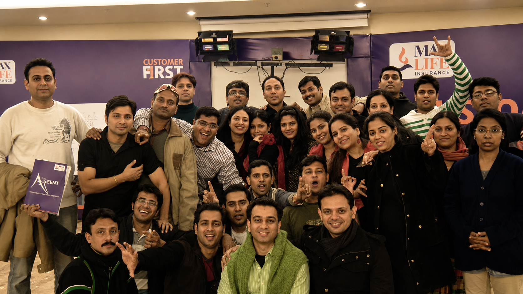 A large team poses together in front of a Max Life Insurance Customer First banner