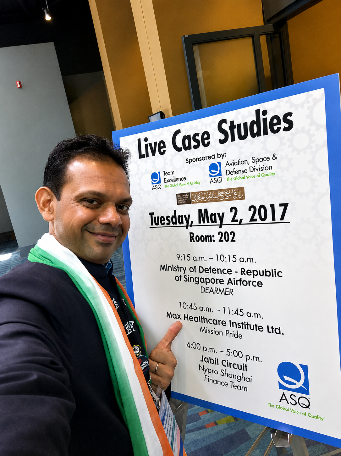 A man smiling beside an ASQ Live Case Studies schedule board listing conference sessions