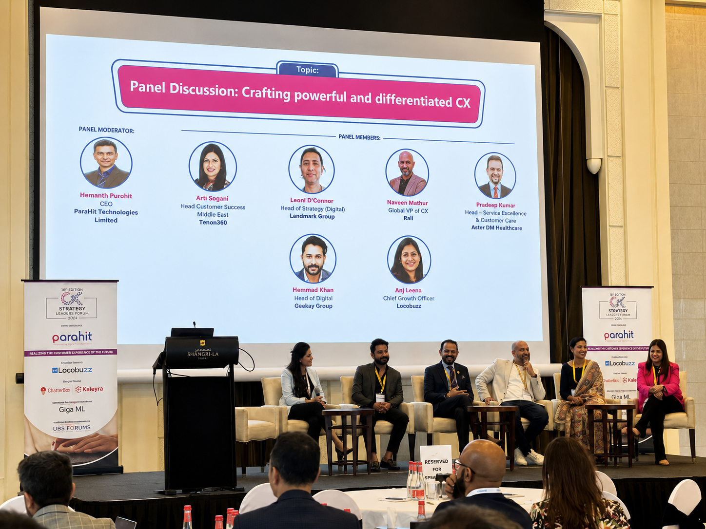 Panel speakers standing on stage in front of a slide listing the Crafting Powerful and Differentiated CX panel members