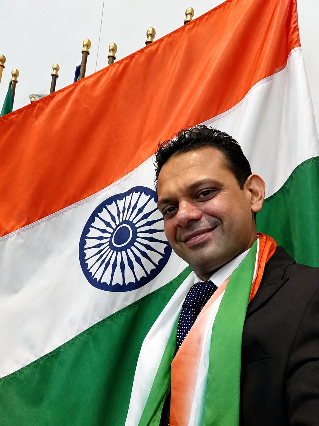 A man smiling for a close-up photo in front of the Indian national flag