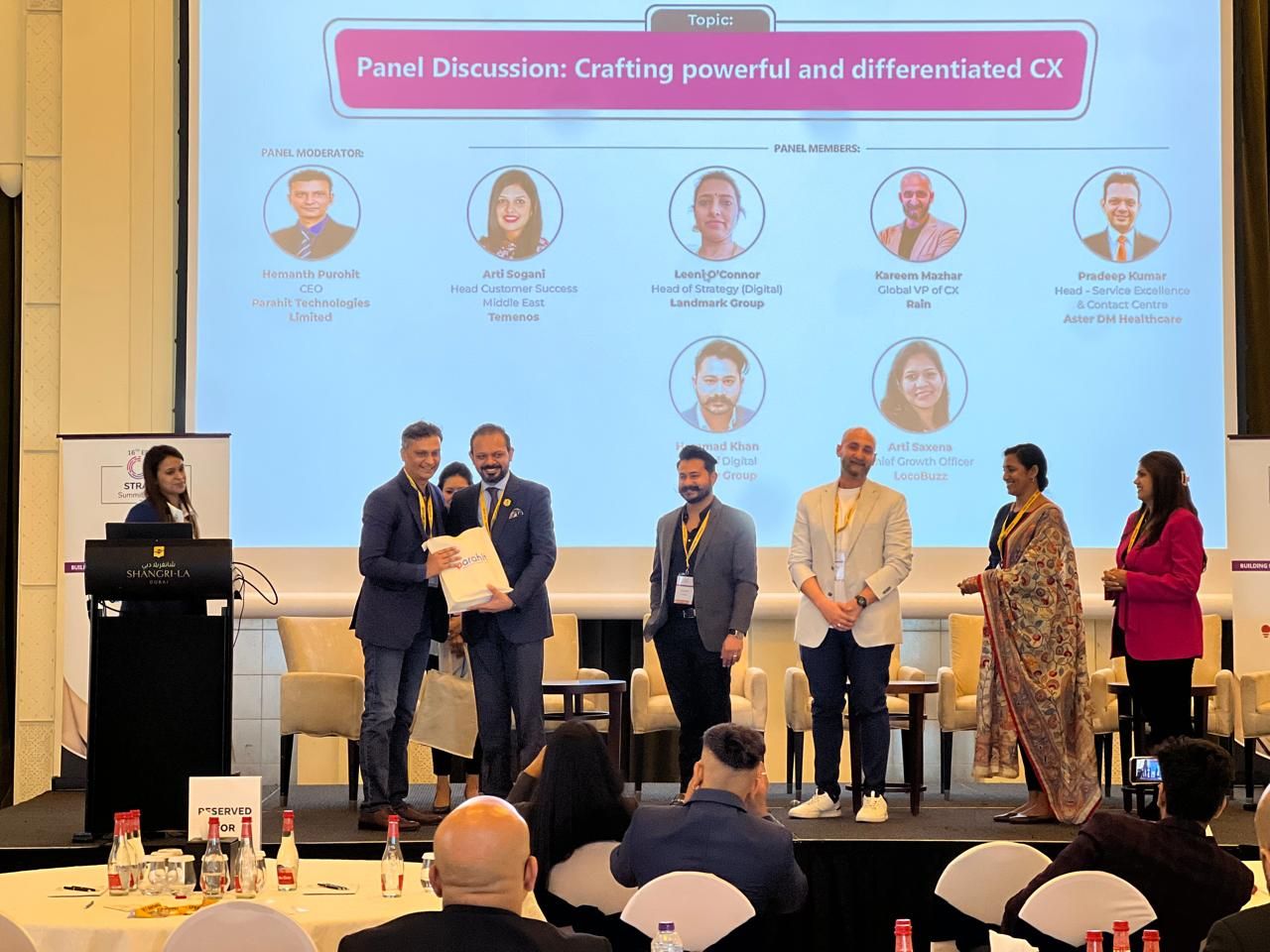 Panel speakers standing on stage in front of a slide titled Panel Discussion: Crafting powerful and differentiated CX