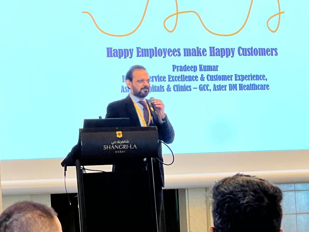 MAGICX founder Pradeep Kumar speaking at a lectern beside a slide reading Happy Employees make Happy Customers